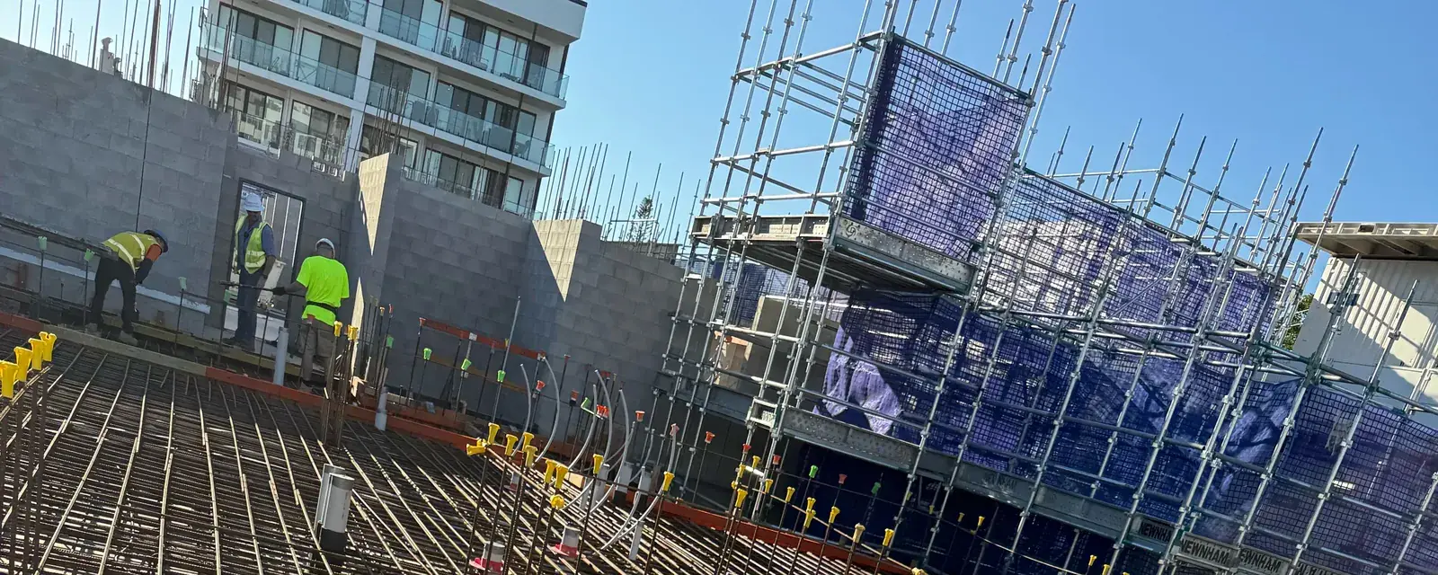 Crew in hi-vis on a large rebar mat deck, scaffold behind