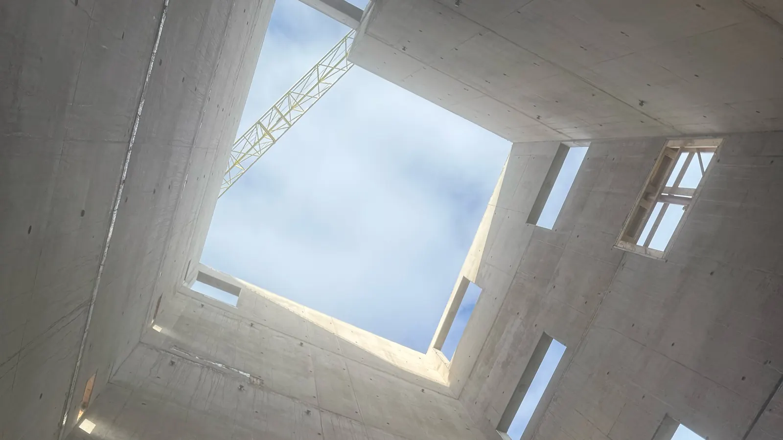 Looking up inside a concrete core to the sky, crane jib overhead