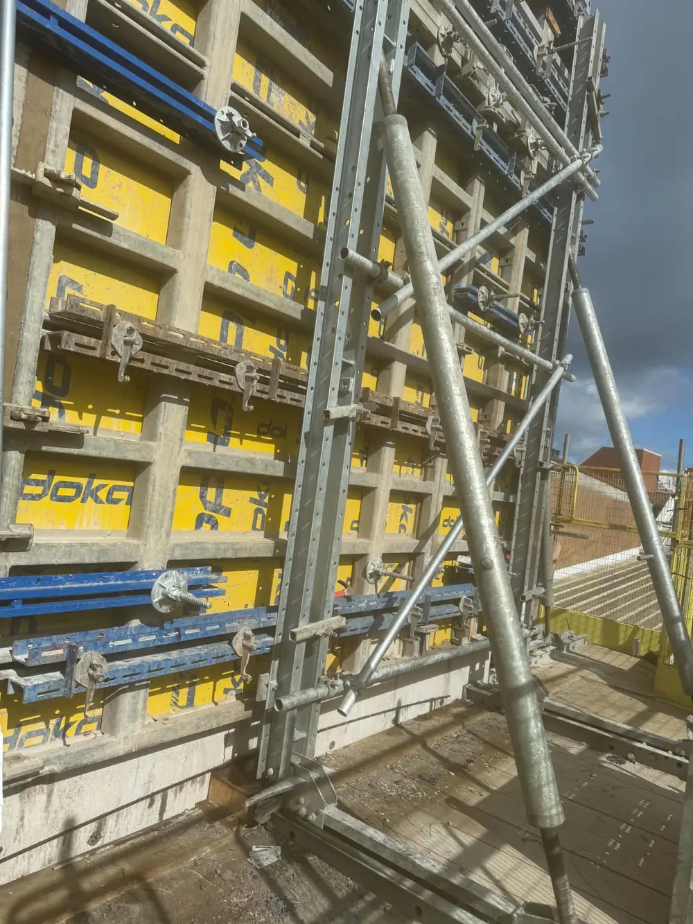 Yellow wall formwork held by push-pull props under a stormy sky